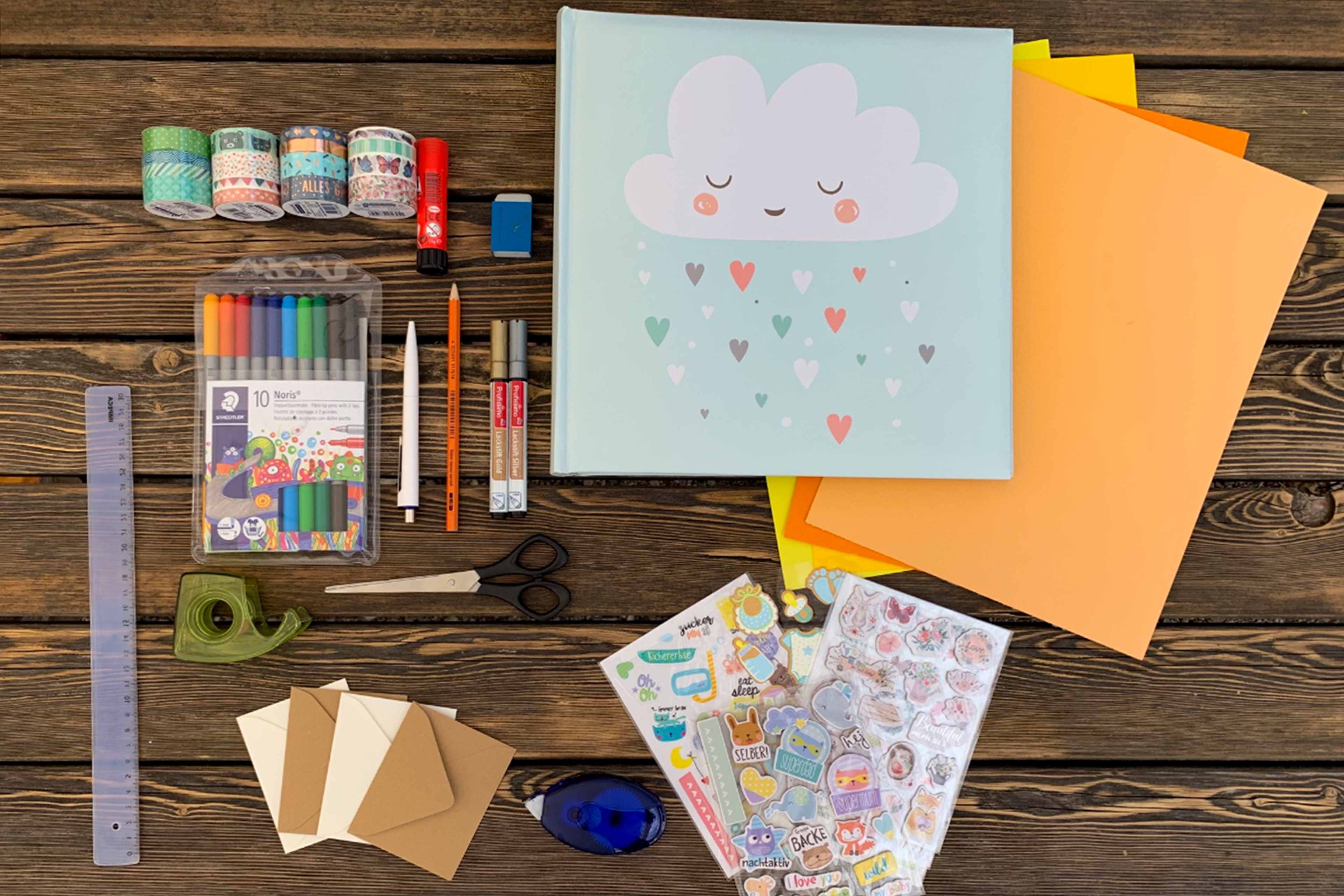 Verschiedenes Kunst- und Bastelmaterial, darunter Buntstifte, Aufkleber, Scheren und ein Notizbuch mit einem Wolkenmotiv.