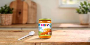 HiPP Bio-Gläschen Karotten mit Mais & Bio-Kalb ab 6. Monat auf Holztisch mit Babylöffel in heller Küche