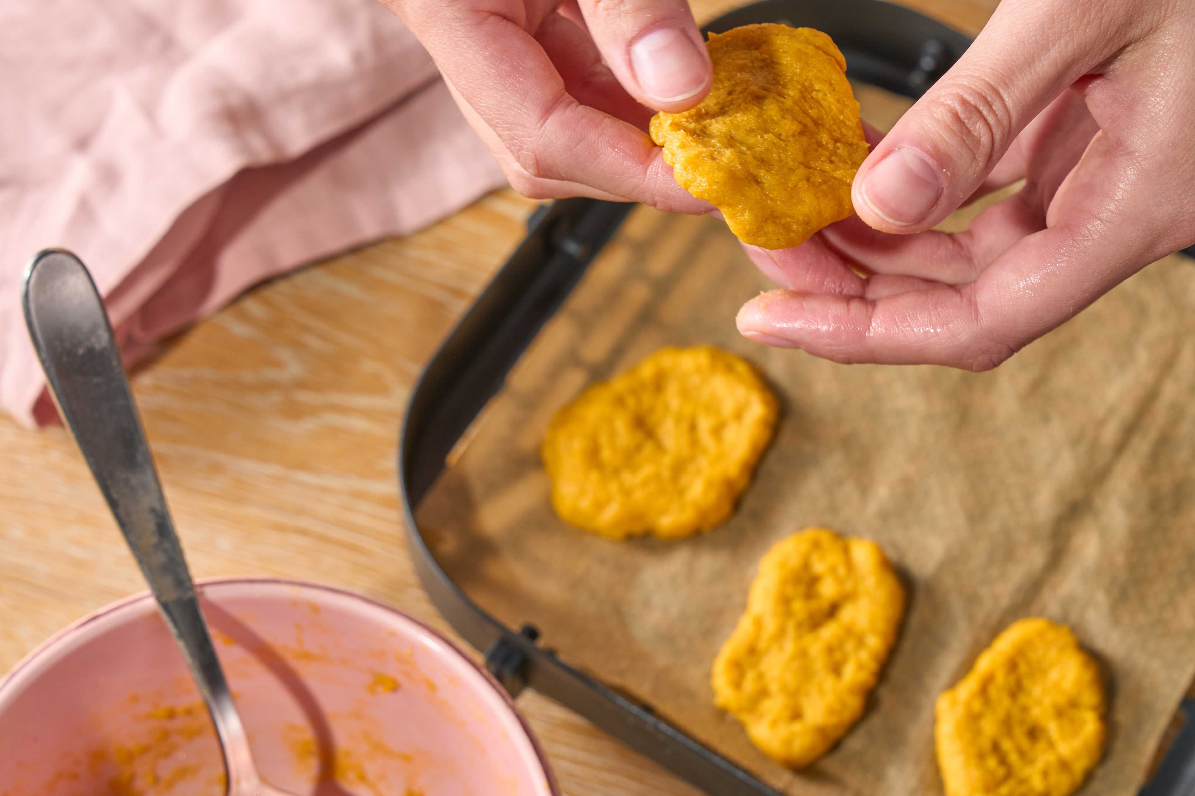 Hände halten ein rundes, gelbliches, unregelmäßig geformtes Gebäckstück und legen es in eine Heißluftfritteuse