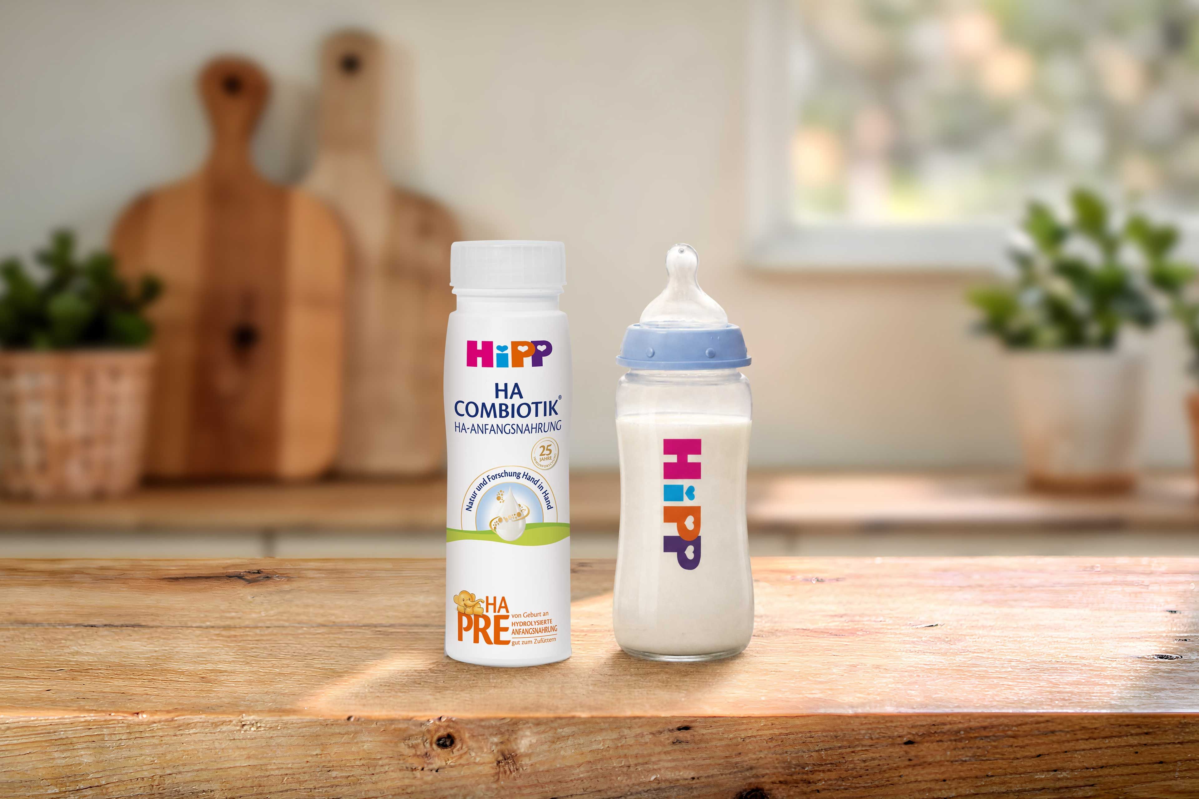 HiPP PRE HA COMBIOTIK® trinkfertige 200ml Flasche neben gefülltem Babyfläschchen auf Holztisch in heller Küche