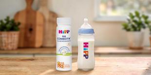 HiPP PRE HA COMBIOTIK® trinkfertige 200ml Flasche neben gefülltem Babyfläschchen auf Holztisch in heller Küche