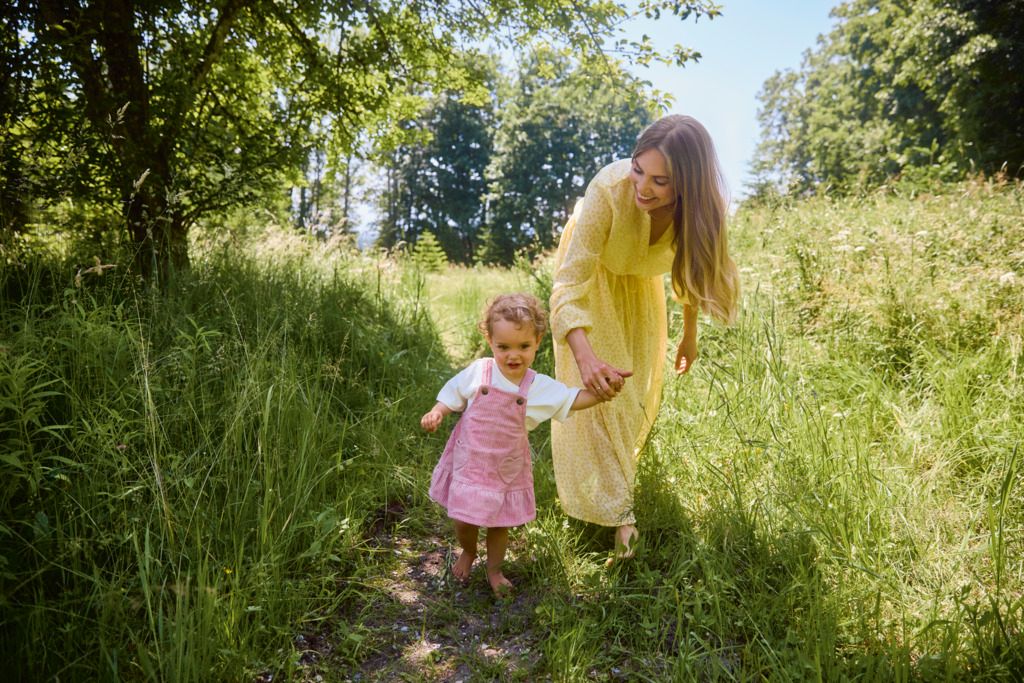 Mutter in gelben Kleid mit Kind an der Hand auf Wiese