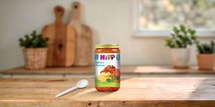 HiPP Bio-Glas Spaghetti Bolognese 250g ab 12 Monaten auf Holztisch mit Löffel in heller Küchenumgebung