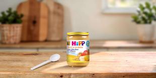 HiPP Feiner Obst-Brei mit Vollkorn im 190g Bio-Gläschen mit Löffel auf Holztisch in heller Küche