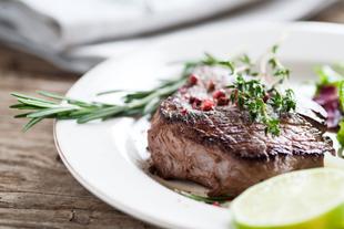 Ein gegrilltes Steak, garniert mit Kräutern und Gewürzen, begleitet von einer Salatbeilage und Limettenspalten.