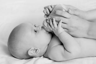 Ein Baby, das von einer Erwachsenenhand mit der Flasche gefüttert wird.