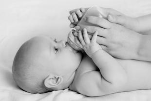 Ein Baby, das von einer Erwachsenenhand mit der Flasche gefüttert wird.