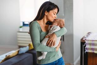 Eine Frau in einem grünen Oberteil küsst sanft ein in ein weißes Tuch gewickeltes Baby.