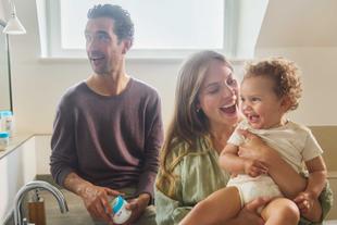 Drei Personen in einer Küche, eine hält ein Baby, eine andere hält eine Dose mit blauem Deckel