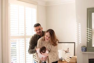 Mum and dad looking down at their baby by a window in a living room