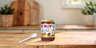 HiPP Bio-Gläschen Pflaume in Apfel mit Vollkorn und Melisse auf Holztisch mit Löffel in heller Küchenumgebung