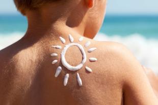 Der Rücken einer Person mit Sonnenschutzmittel in Form einer Sonne, mit dem Meer im Hintergrund.