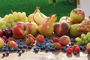 Eine Vielzahl von frischen Früchten, darunter Äpfel, Bananen, Trauben, Birnen und Blaubeeren, die auf einer Holzfläche angeordnet sind.