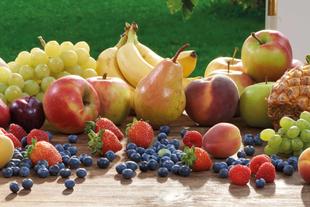 Eine Vielzahl von frischen Früchten, darunter Äpfel, Bananen, Trauben, Birnen und Blaubeeren, die auf einer Holzfläche angeordnet sind.