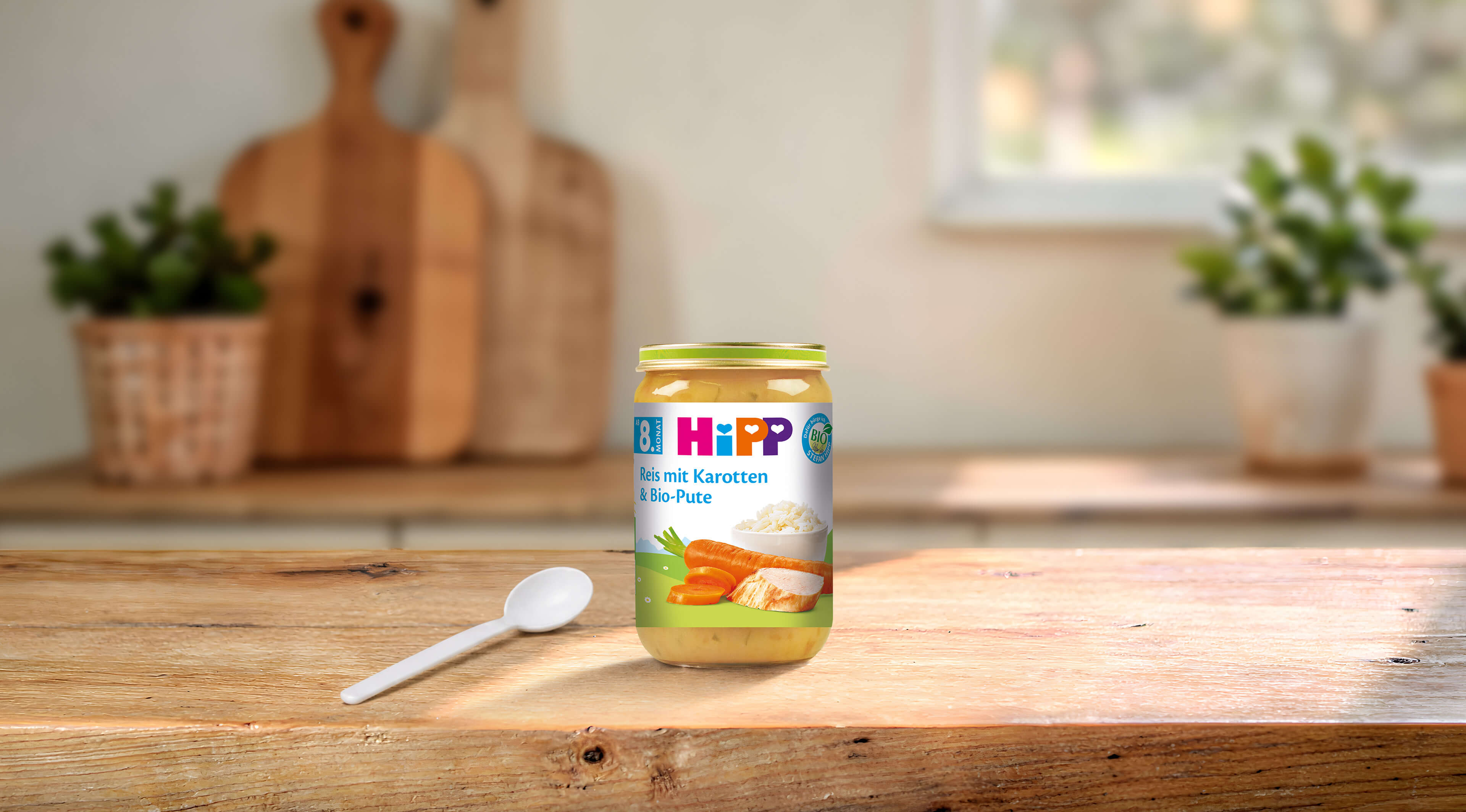 HiPP Bio-Gläschen Reis mit Karotten und Bio-Pute ab dem 8. Monat auf Holztisch mit Löffel in heller Küche