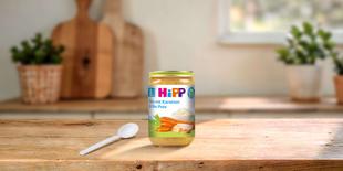 HiPP Bio-Gläschen Reis mit Karotten und Bio-Pute ab dem 8. Monat auf Holztisch mit Löffel in heller Küche