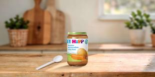 HiPP Bio-Gläschen Kartoffel-Gemüse mit Bio-Rind ab dem 8. Monat auf Holztisch in heller Familienküche mit Löffel daneben