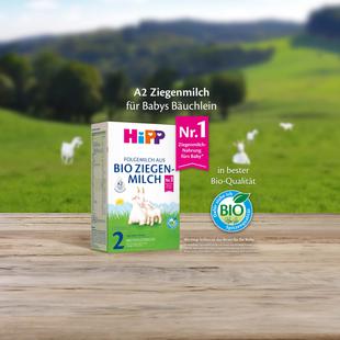 HiPP 2 Folgemilch aus Bio Ziegenmilch Packung auf Holztisch vor grüner Weidelandschaft mit Ziegenmotiv