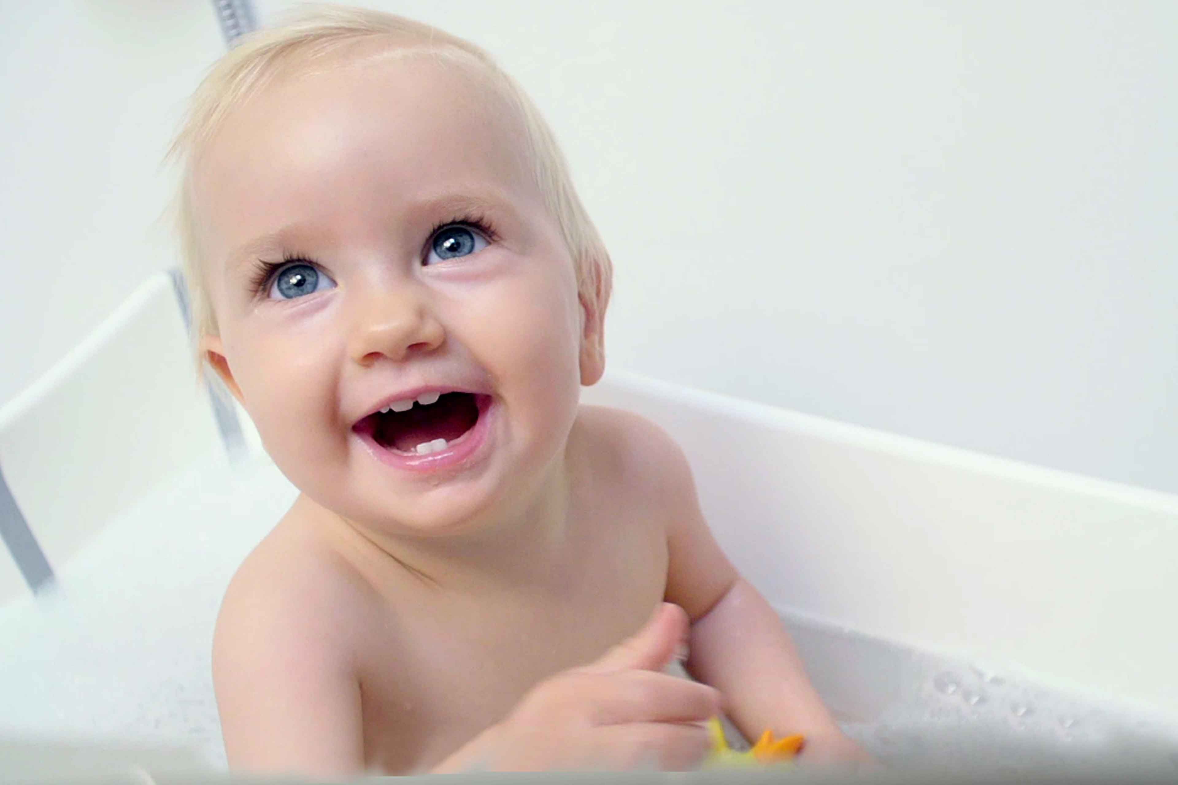 Kleinkind mit nassen Haaren sitzt in einer Badewanne und hält einen Gegenstand in der Hand.