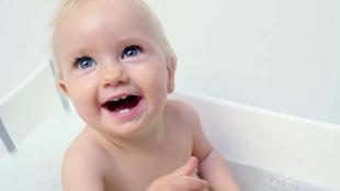 Ein fröhliches Baby in einer Badewanne, mit Blasen um sich herum, das mit großen Augen nach oben schaut.