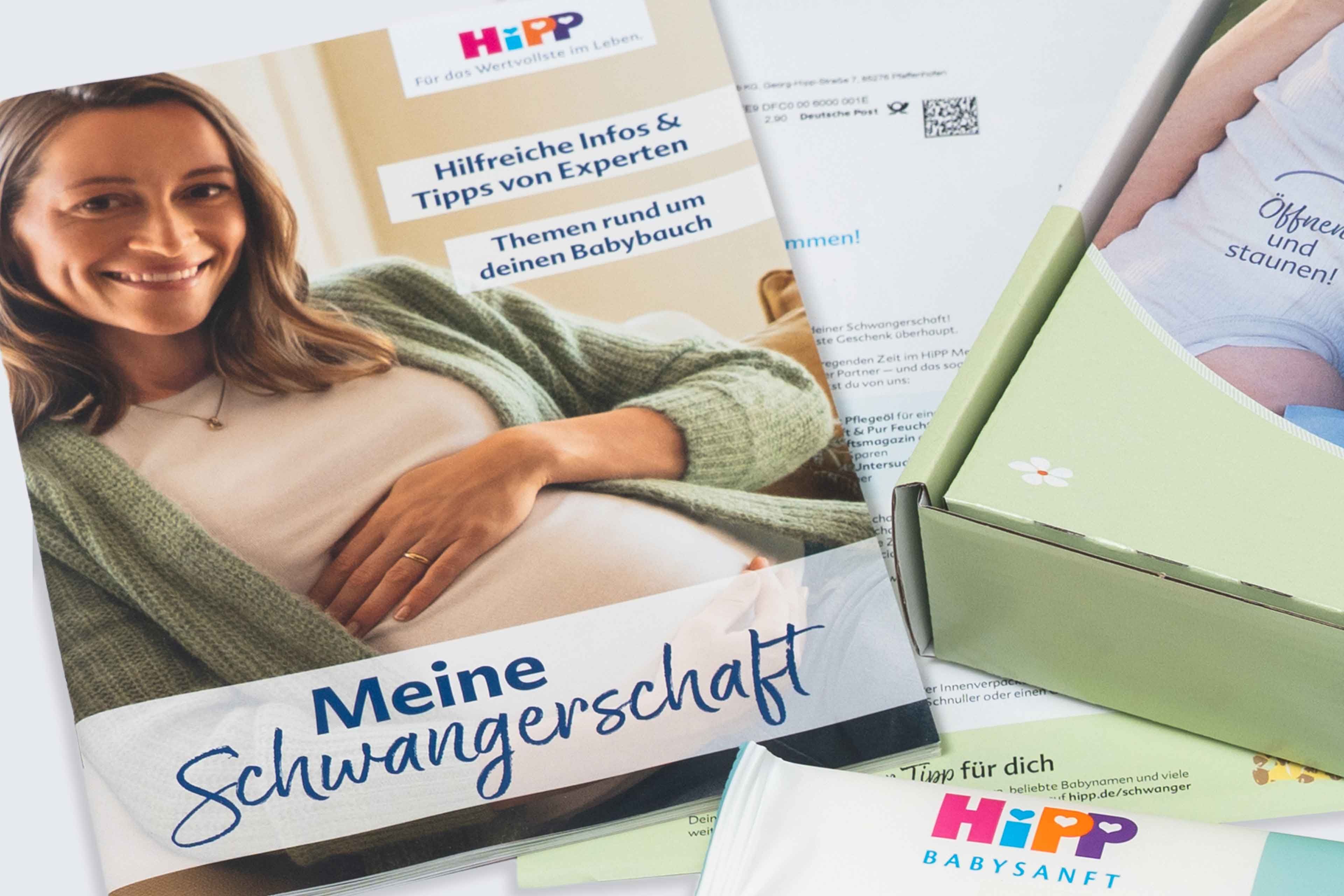 Schwangere Frau mit grünem Strickcardigan hält ihren Bauch vor einem Magazin mit der Überschrift 'Meine Schwangerschaft'