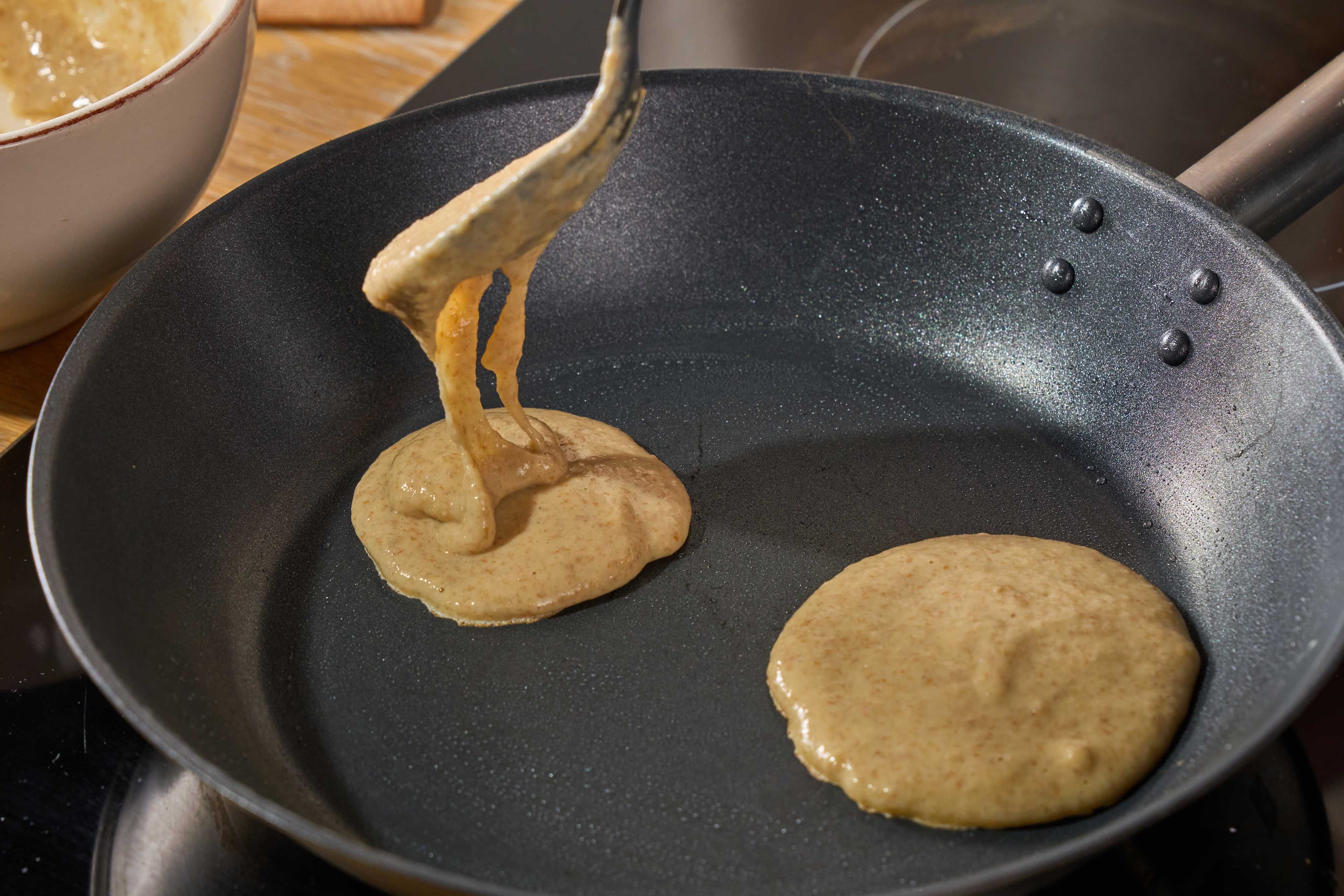 Teig wird aus einem Löffel in eine Pfanne mit zwei kleinen Teigfladen gegossen