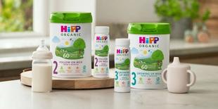 HiPP Organic follow on and growing up milks on a kitchen worktop next to a bottle of milk and a sippy cup