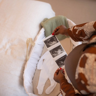 Top down view of mum with bump holding ultrasound photos over bassinet with a baby grow in