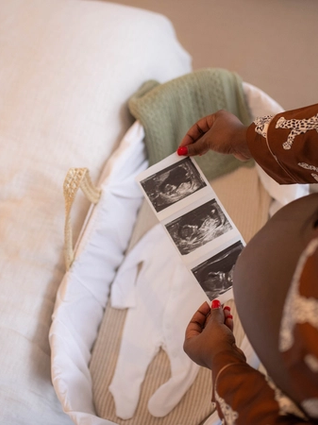 Top down view of mum with bump holding ultrasound photos over bassinet with a baby grow in