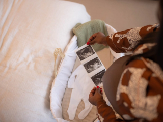 Top down view of mum with bump holding ultrasound photos over bassinet with a baby grow in