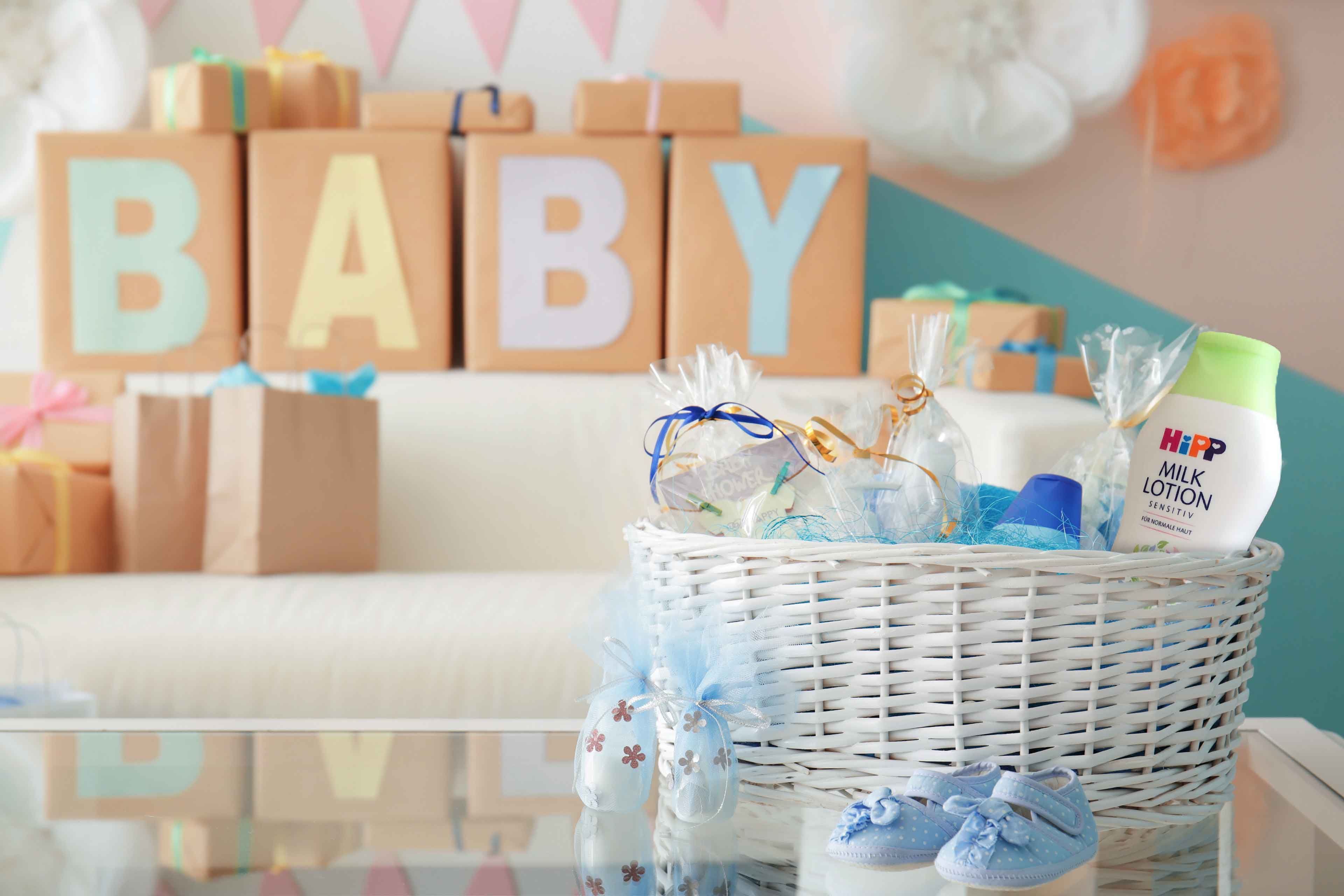 Weißer Korb mit Babyartikeln und blauen Babyschuhen vor Geschenkpaketen mit großen Buchstaben, die BABY bilden
