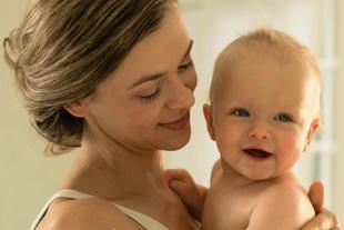Lächelnde Mutter hält ihr fröhliches Baby nah am Körper, inniger Moment von Nähe und Geborgenheit