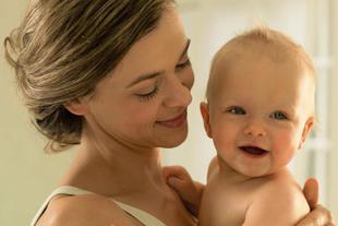 Lächelnde Mutter hält ihr fröhliches Baby nah am Körper, inniger Moment von Nähe und Geborgenheit