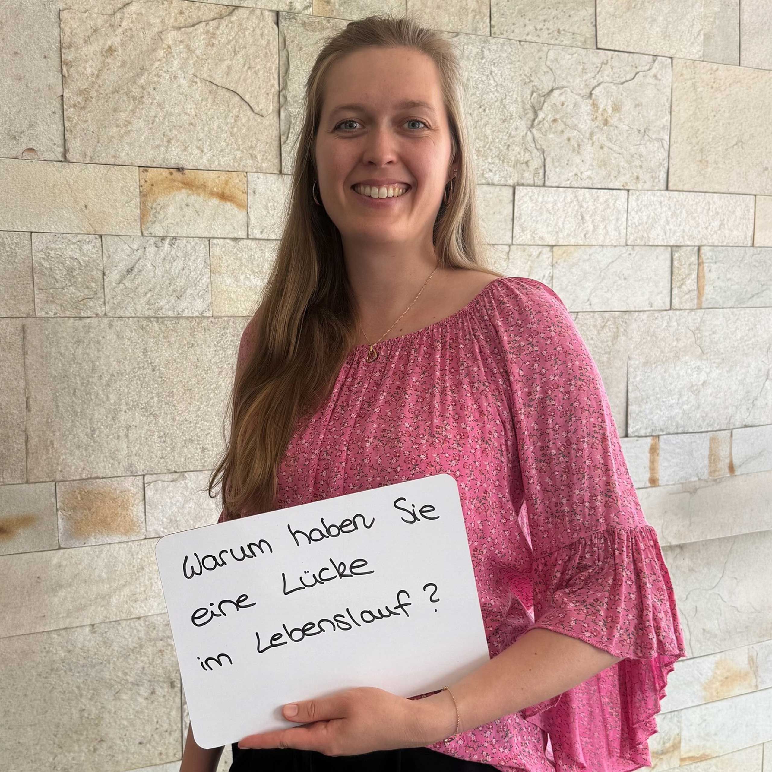 Eine HiPP Mitarbeiterin hält ein Schild mit der Aufschrift 'Warum haben Sie eine Lücke im Lebenslauf'