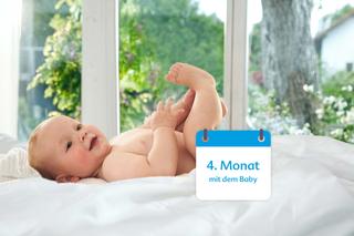 Ein Baby, vermutlich 4 Monate alt, liegt auf einem Bett mit einer weißen Decke neben einem Kalender mit der Aufschrift "4. Monat mit dem Baby".