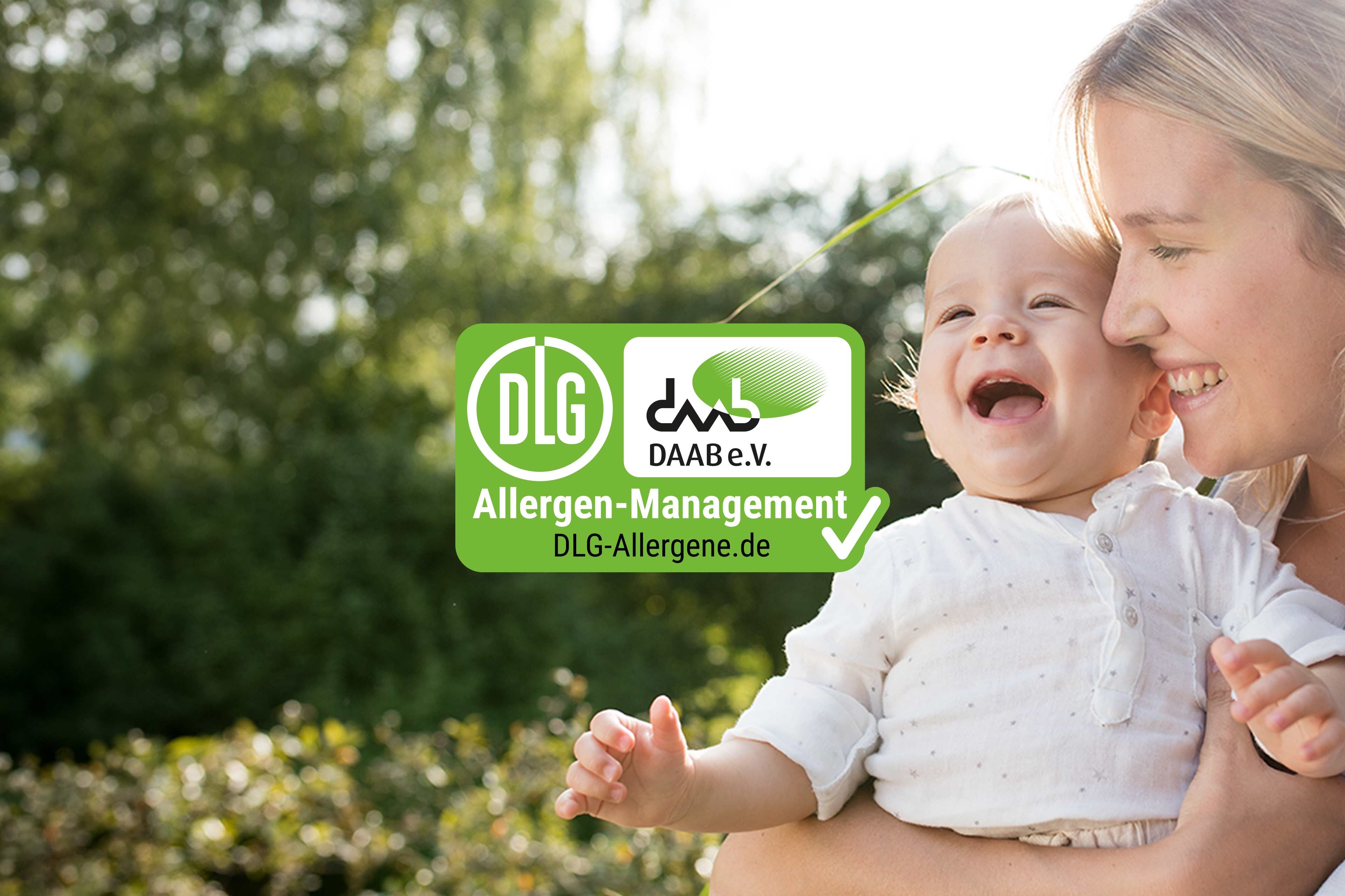Lachendes Baby im Arm der Mutter im Grünen, daneben ein DLG-Allergen-Management-Siegel für sicheres Allergenmanagement.