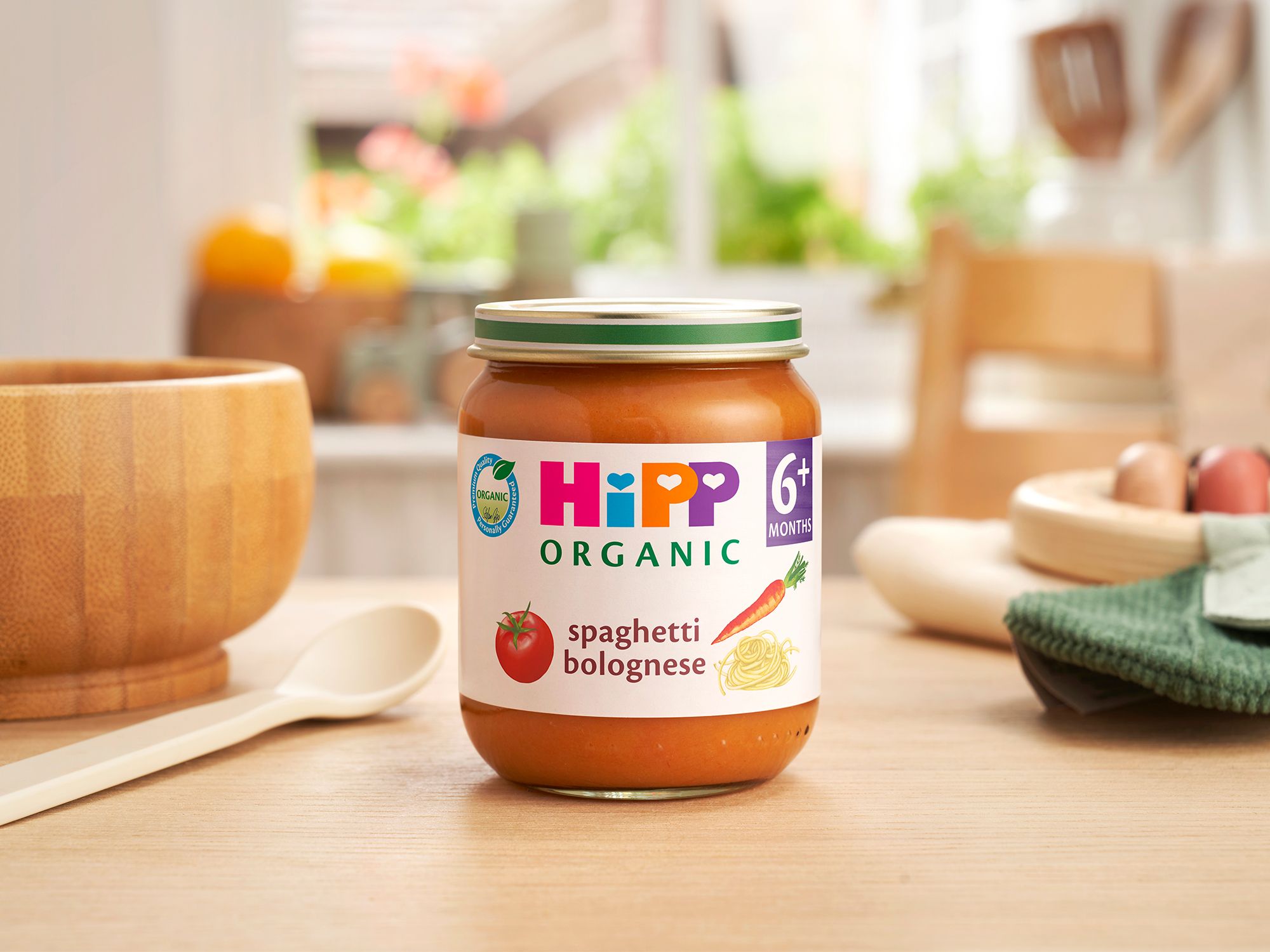 HiPP Organic Spaghetti Bolognese 6 months+ on a dining table next to a bowl and spoon