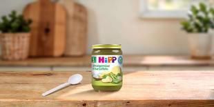 HiPP Bio-Gläschen „Spinatgemüse in Kartoffeln“ ab 5. Monat auf Holztisch, daneben ein Löffel in heller Küchenumgebung