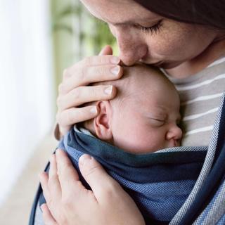 Nahaufnahme des Gesichts eines Babys, das in ein blaues Tuch gebettet ist und von der Hand eines Erwachsenen gehalten wird.