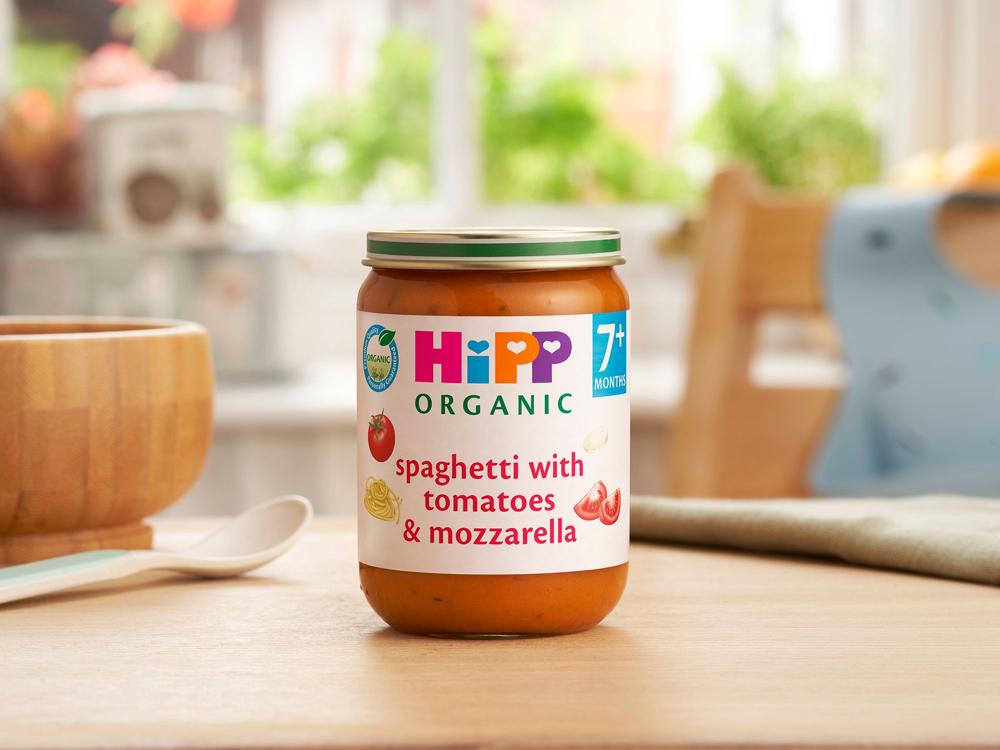 HiPP Organic Spaghetti with tomatoes & mozzarella on a dining table next to a bowl and spoon