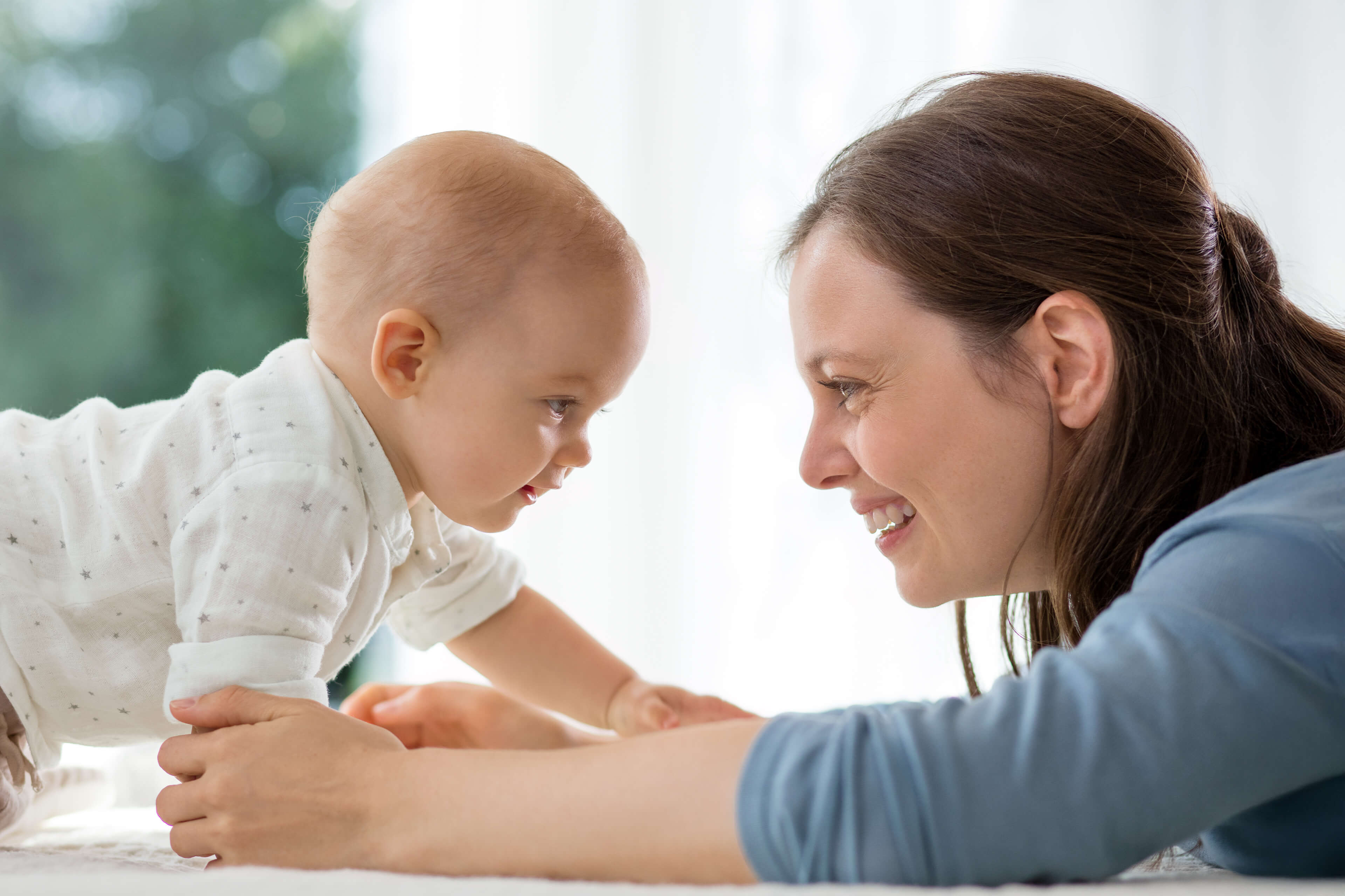 Ein zärtlicher Moment zwischen einer Mutter und ihrem Baby, in dem das Baby die Hand ausstreckt, um das Gesicht der Mutter zu berühren, und die Mutter zärtlich lächelt.