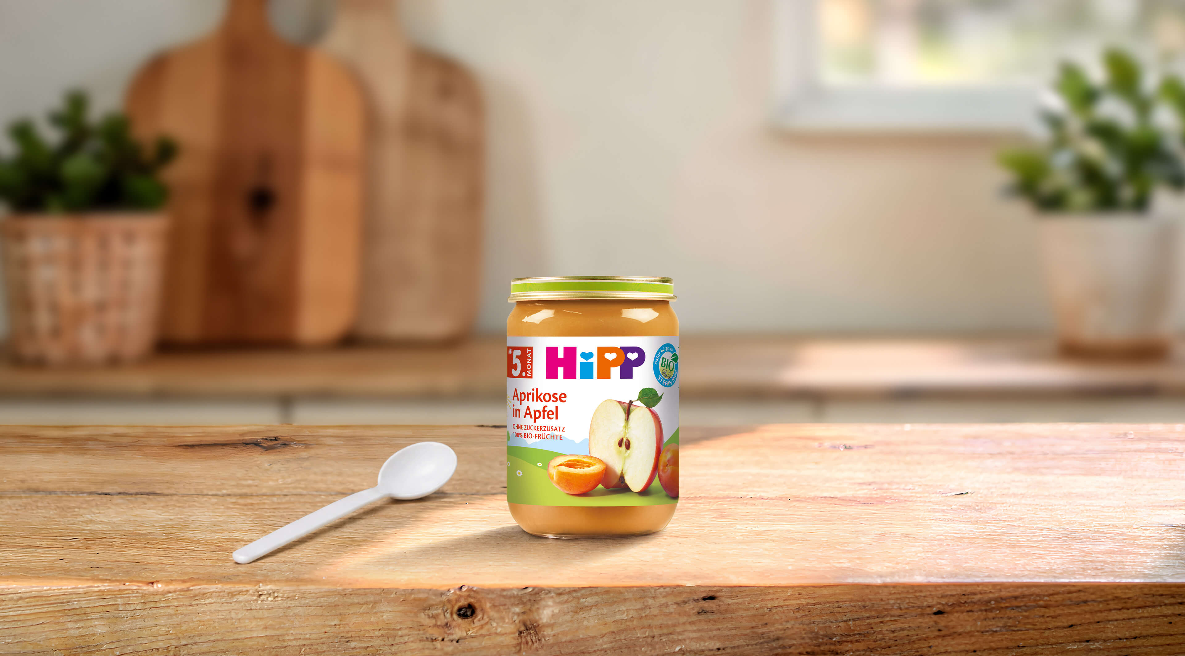 HiPP Bio Fruchtpüree Aprikose in Apfel 190g Glas auf Holztisch mit Löffel in heller Küche