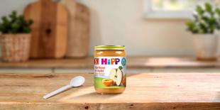 HiPP Bio Fruchtpüree Aprikose in Apfel 190g Glas auf Holztisch mit Löffel in heller Küche