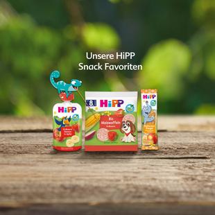 Drei HiPP-Snackprodukte auf Holzuntergrund vor unscharf grünem Hintergrund mit Text 'Unsere HiPP Snack Favoriten'