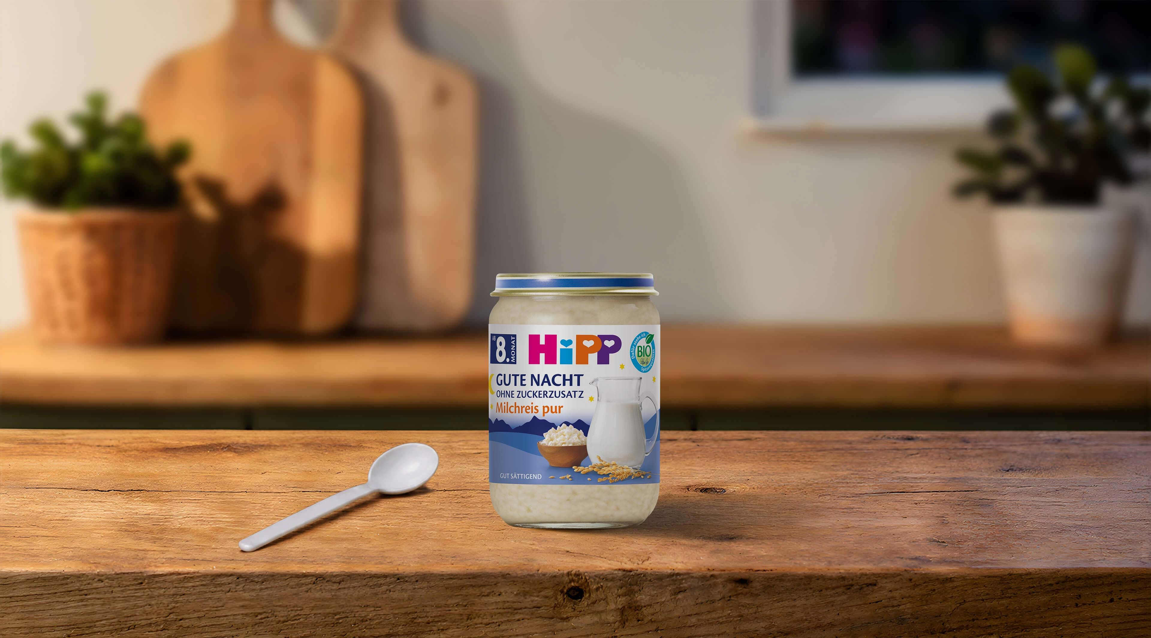 HiPP Gute Nacht Milchreis pur Bio-Abendbrei im Glas mit Löffel auf einem Holztisch in gemütlicher Küchenatmosphäre