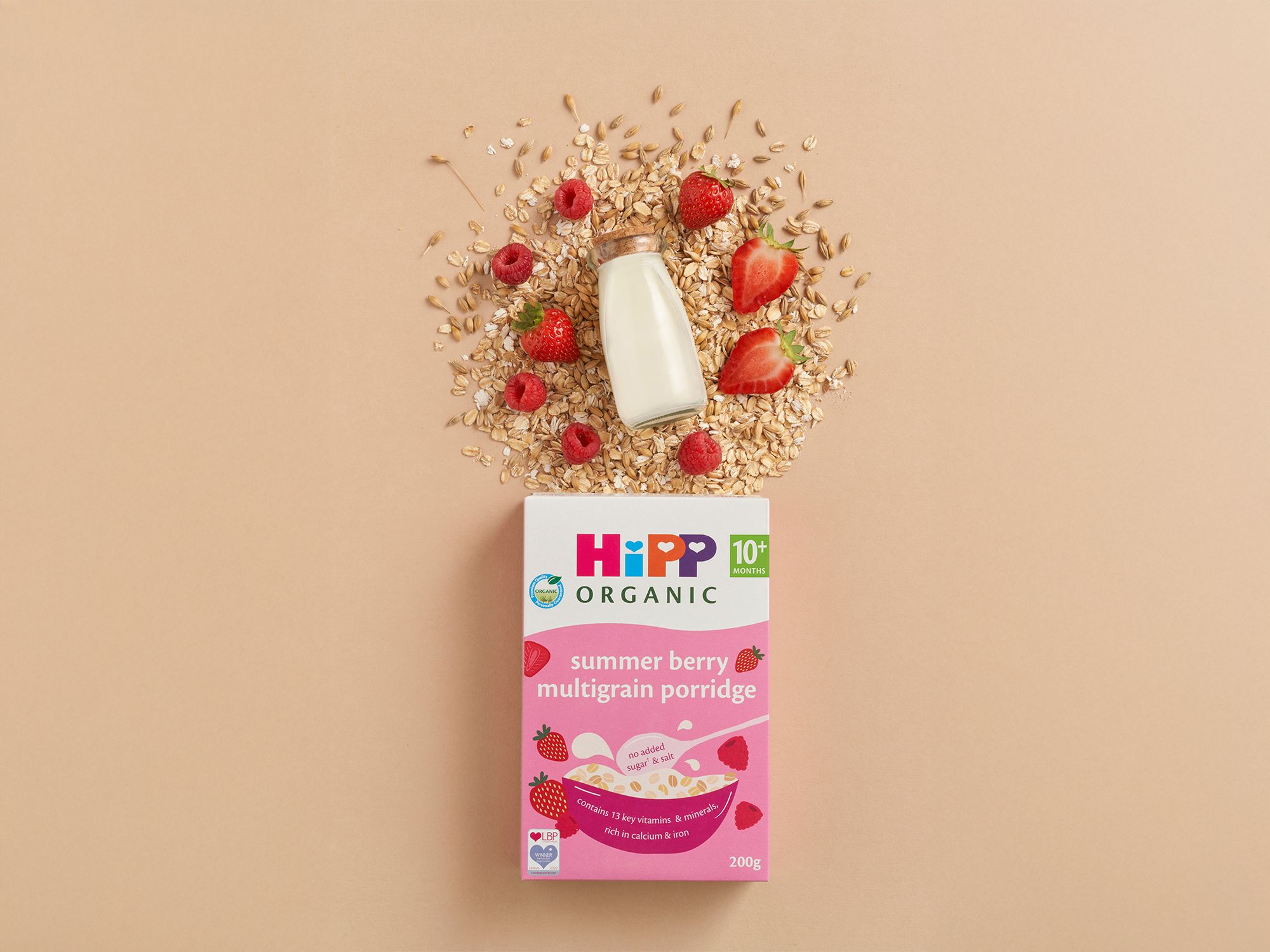 HiPP Organic Summer Berry Multigrain Porridge box with milk, oats, strawberries and raspberries on a neutral background