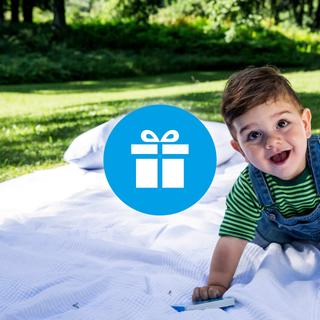 Lachendes Baby auf einer Picknickdecke im Grünen, daneben ein Geschenk-Symbol als Hinweis auf Gewinnspiele