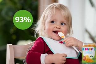 Lachendes Baby im Hochstuhl mit HiPP-Lätzchen isst 100% pflanzlich Spaghetti mit Linsen-Bolognese, daneben grüner Kreis mit „93 %“.