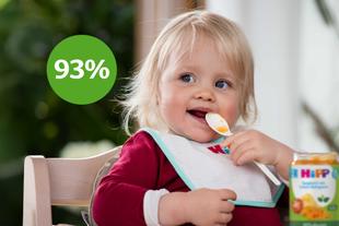 Lachendes Baby im Hochstuhl mit HiPP-Lätzchen isst 100% pflanzlich Spaghetti mit Linsen-Bolognese, daneben grüner Kreis mit „93 %“.