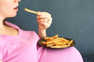 Eine Person in einem rosa Hemd, die einen Teller mit Pommes frites in der Hand hält und einen sichtbaren Schwangerschaftsbauch hat.